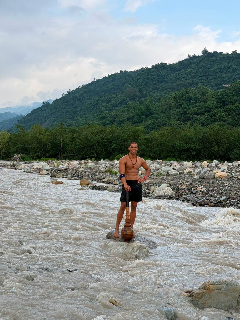 Raja Yadav standing on a river rock with a gada